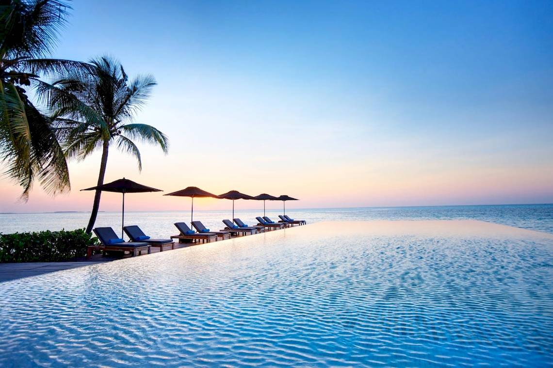 Sonnenuntergang am Infinity-Pool des LUX South Ari Atoll Hotels mit Sonnenliegen und Schirmen
