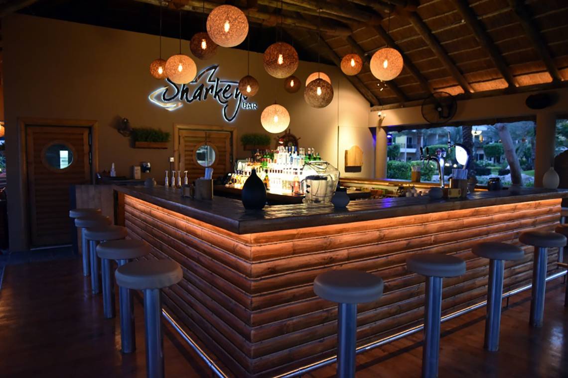 Innenansicht der Sharkey Bar im Fujairah Rotana Resort & Spa mit Holztheke und Barhockern.