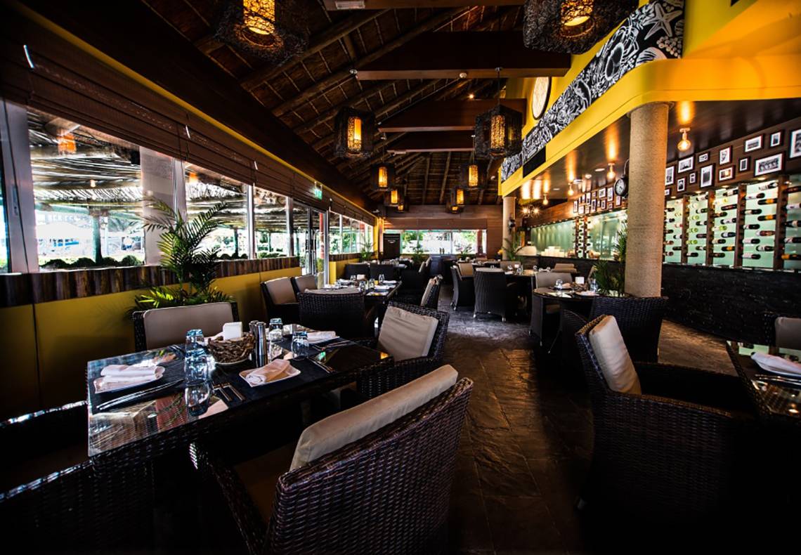 Innenansicht des Restaurants im Fujairah Rotana Resort & Spa mit runden Tischen und Stühlen.