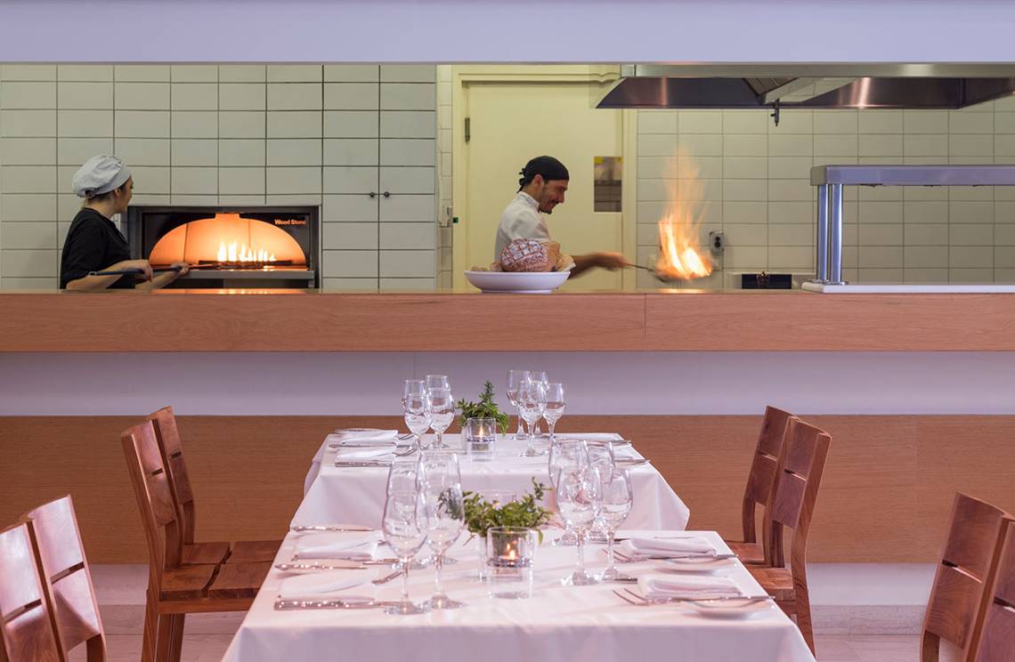 Restaurantszene im Avra Imperial Hotel mit Koch, der Flammen erzeugt, und Kellnerin hinter Ofen