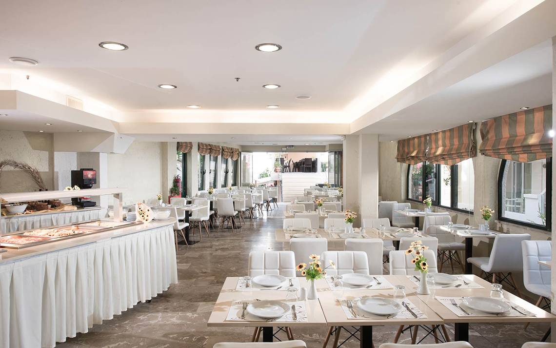 Frühstücksraum des Odyssia Beach Hotels mit weißen Tischen und Stühlen.