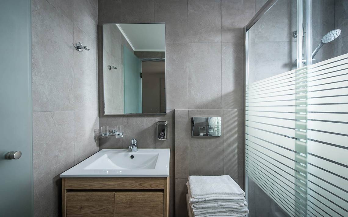 Ein Badezimmer im Odyssia Beach Hotel mit grauen Fliesen, einem Waschbecken, einem Spiegel und einer Glasdusche.