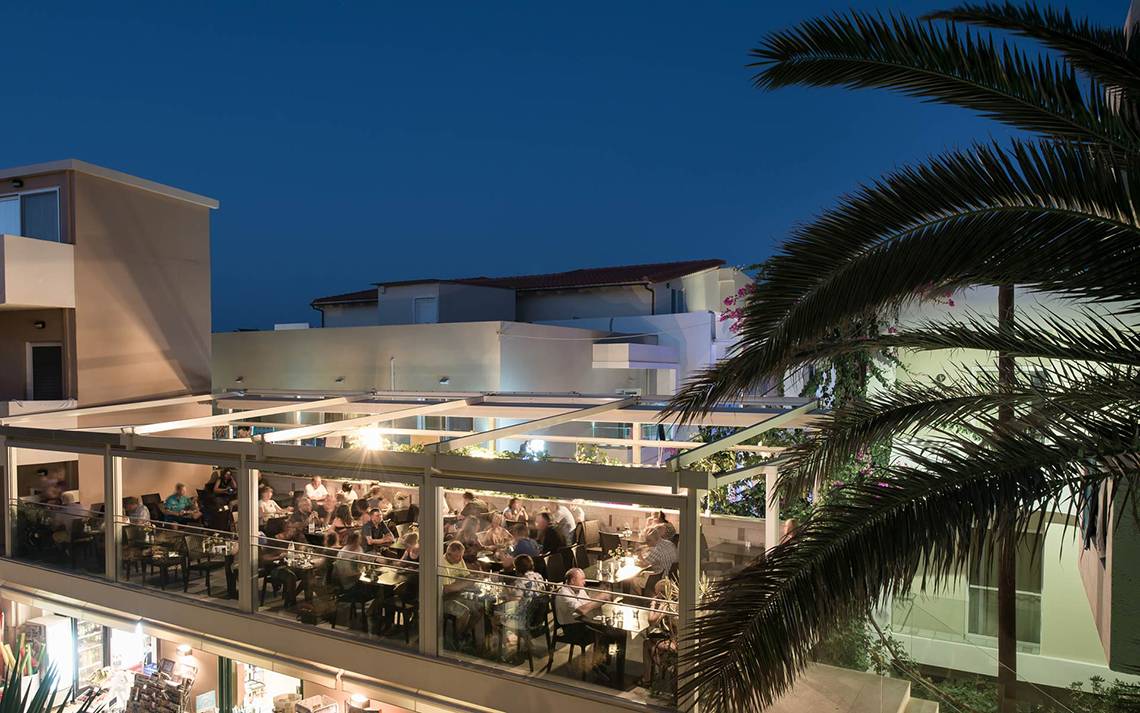 Abendessen auf der Terrasse des Odyssia Beach Hotels mit vielen Gästen und Palmen im Vordergrund.