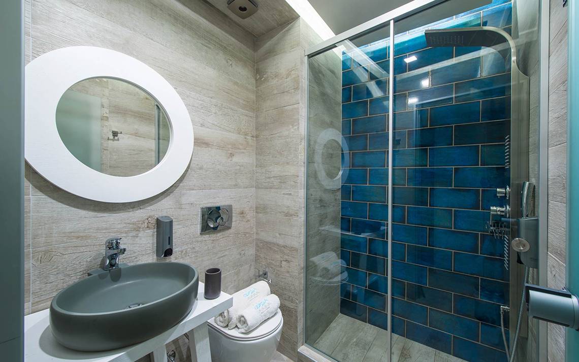 Badezimmer im Odyssia Beach Hotel mit blauen Fliesen, Dusche, Toilette und Waschbecken.