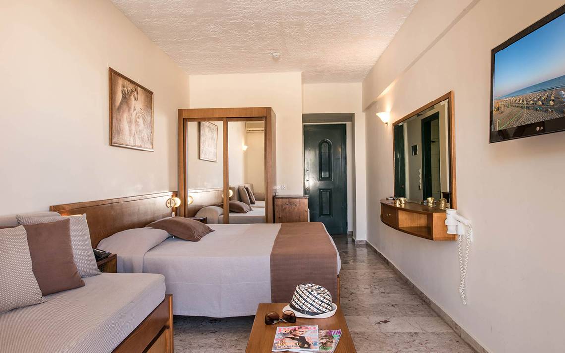Doppelbett-Hotelzimmer im Odyssia Beach Hotel mit Fernseher, Spiegel und Sofa.