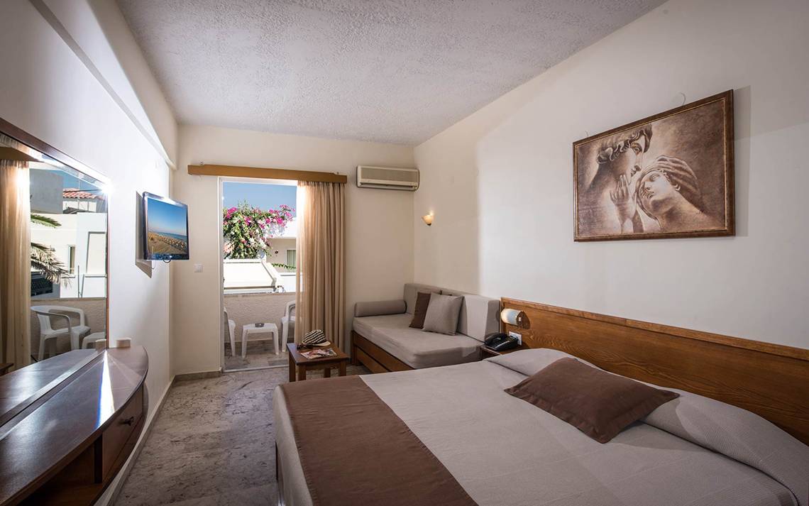 Innenansicht eines Hotelzimmers im Odyssia Beach Hotel mit Doppelbett, Sofa und Balkon.