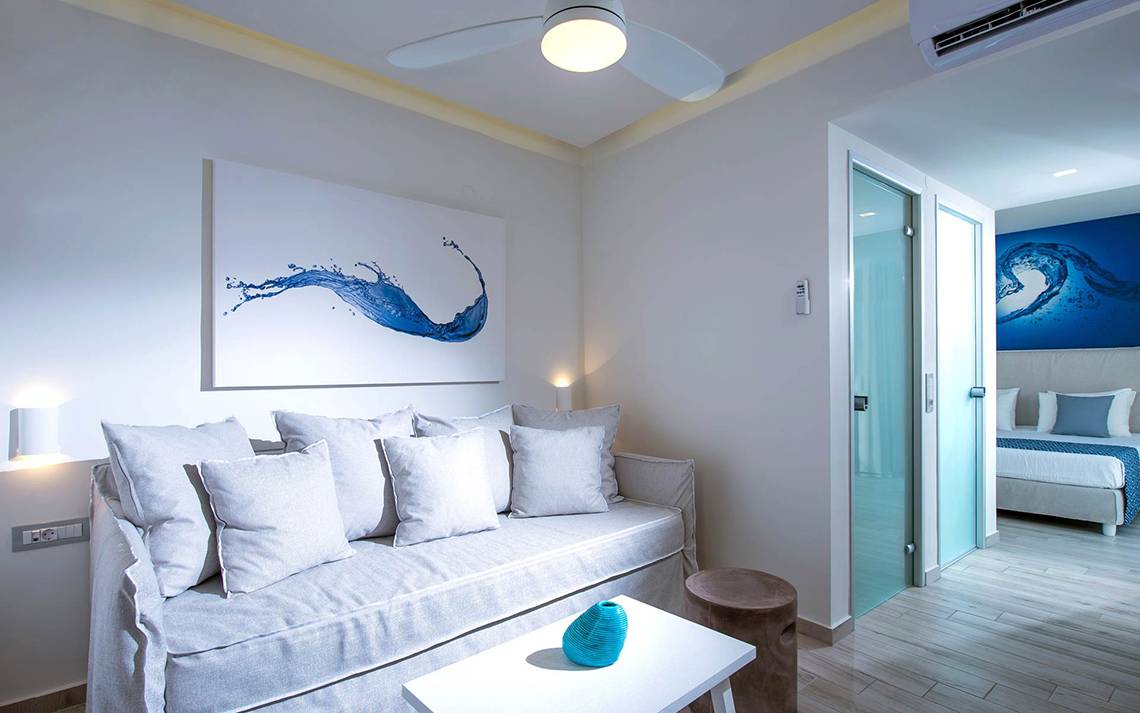 Wohnbereich des Odyssia Beach Hotels mit Schlafsofa, Tisch, Gemälde und Schlafzimmer