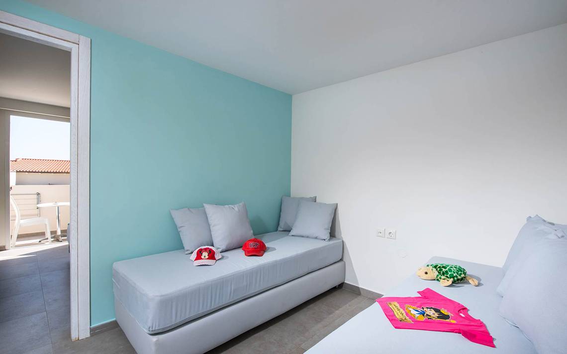 Kinderzimmer im Odyssia Beach Hotel mit zwei Betten, Kissen, und Spielzeug.