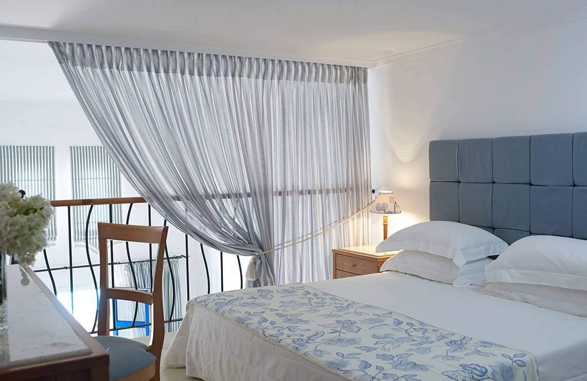 Schlafzimmer im Mitsis Norida Beach Hotel mit Blick auf den Balkon und einem Bett mit weißen Kissen.