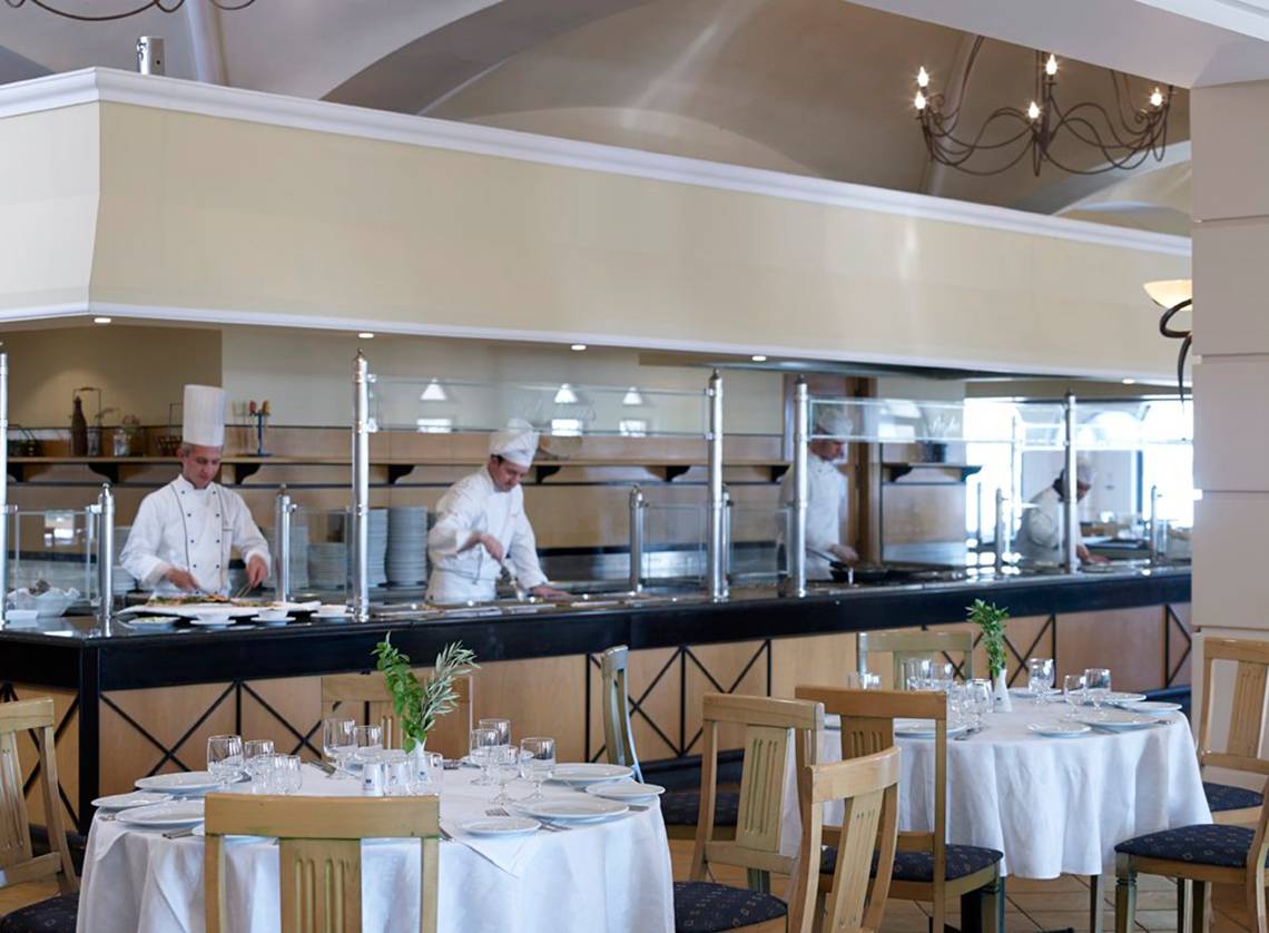 Im Mitsis Norida Beach Hotel Restaurant sehen wir ein Buffet mit Köchen, die hinter einer Glaswand arbeiten.