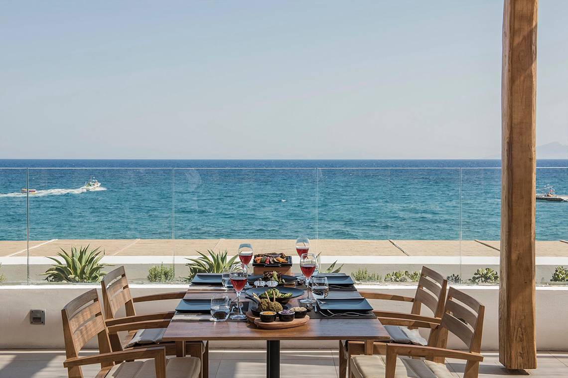 Terrasse des Mitsis Norida Beach Hotels mit Blick auf das Meer und zwei Boote auf dem Wasser.