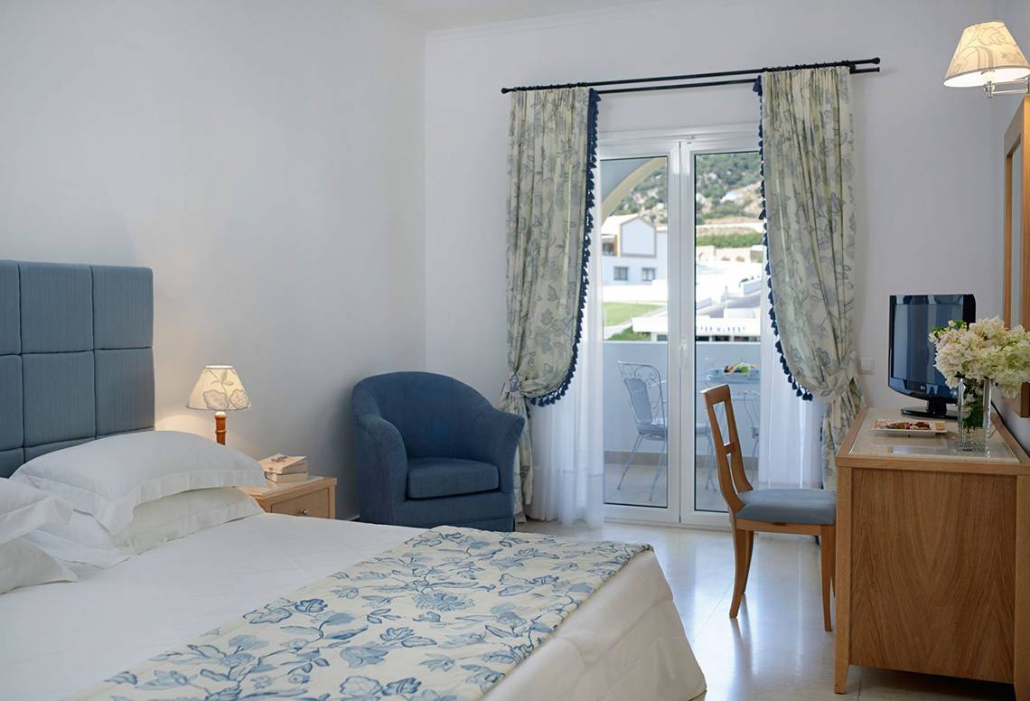 Schlafzimmer im Mitsis Norida Beach Hotel mit Bett, Stuhl, Schreibtisch und Balkon