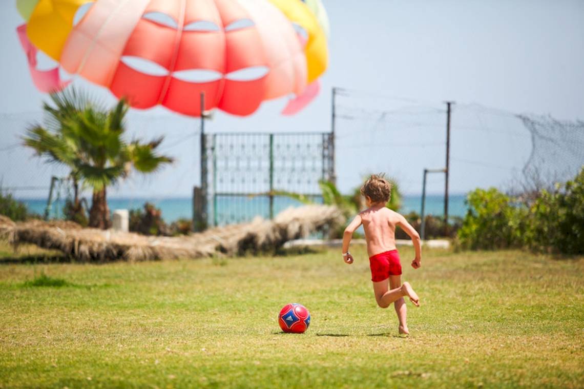 Ein junger Junge spielt mit einem Fußball am Strand, während ein Parasailing-Ballon im Hintergrund schwebt.