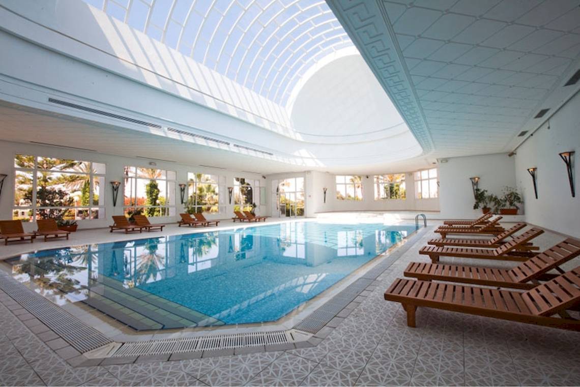 Innenbereich des Schwimmbads im El Mouradi Mahdia Hotel mit Pool und Sonnenliegen.