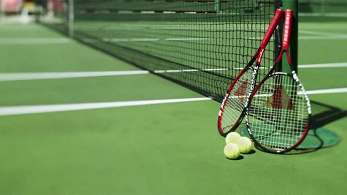 Tennisschläger und Bälle auf einem Tennisplatz neben einem Netz.
