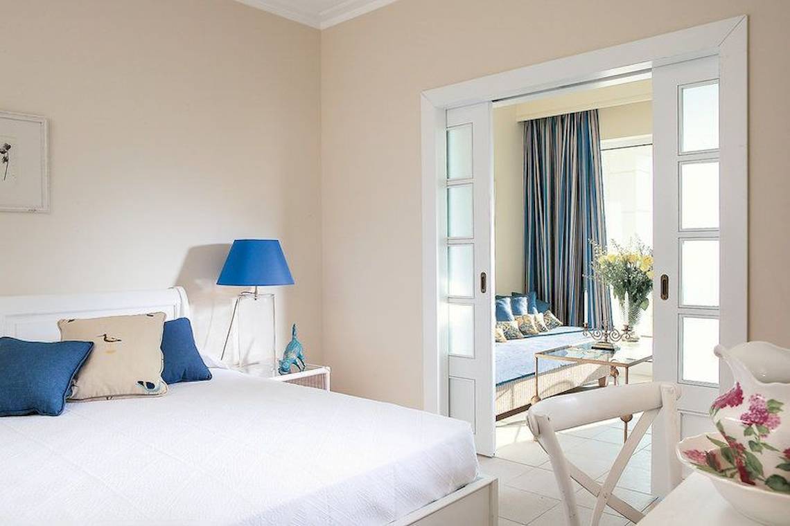 Schlafzimmer im Grecotel La Riviera & Aqua Park mit weißem Bett und blauen Kissen.