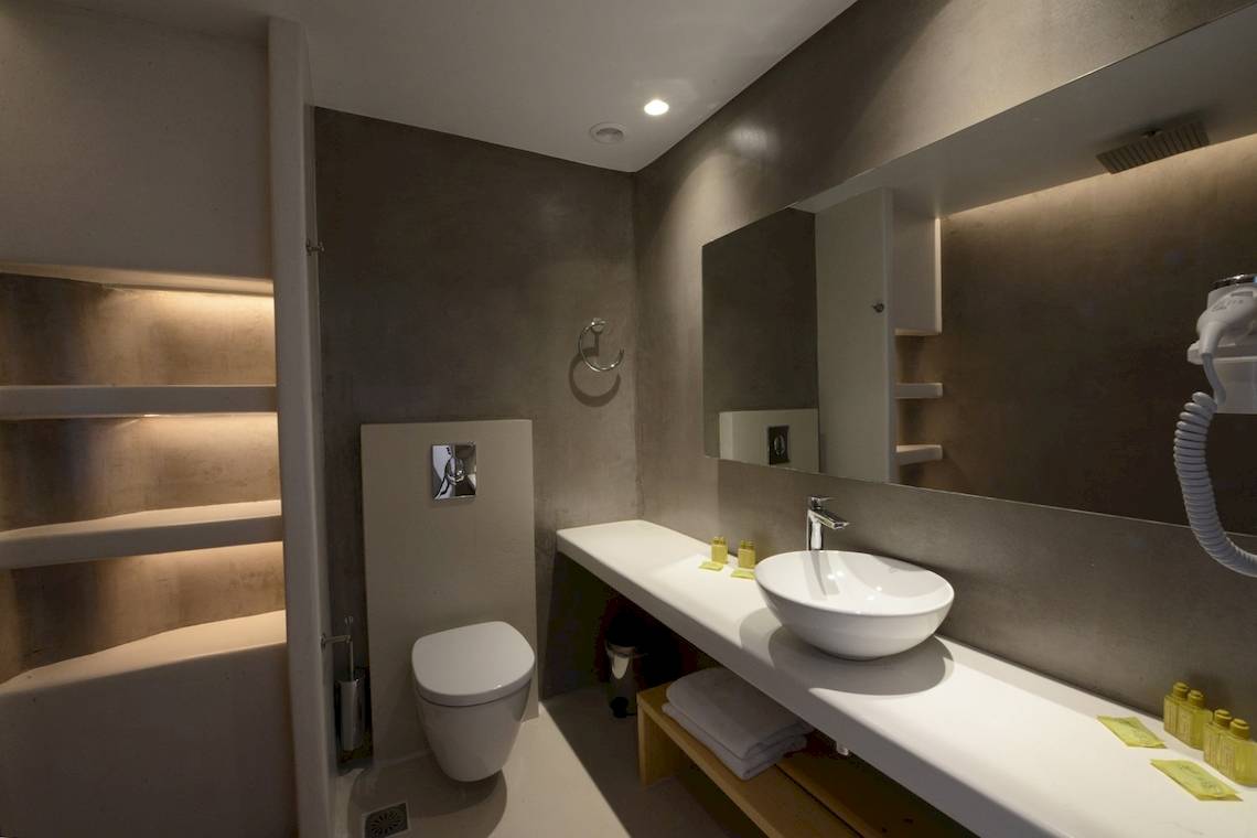 Badezimmer im MykonosView Hotel mit grauen Wänden, weißem Waschbecken und Toilette.