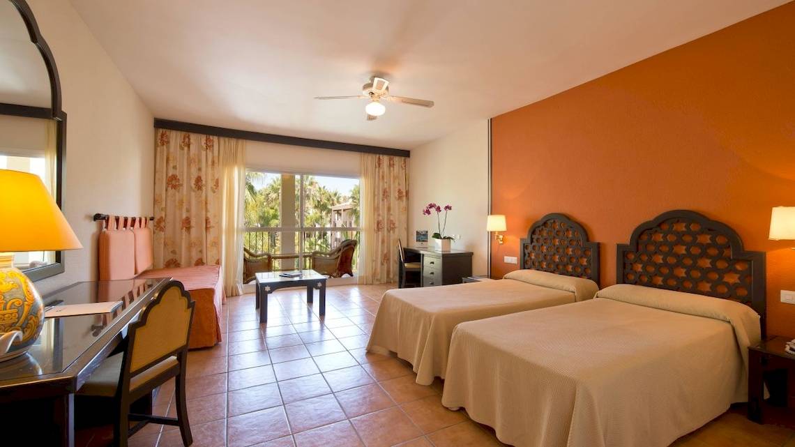 Doppelzimmer im Bluebay Banus Hotel mit zwei Betten, Schreibtisch, Lampe und Balkon.