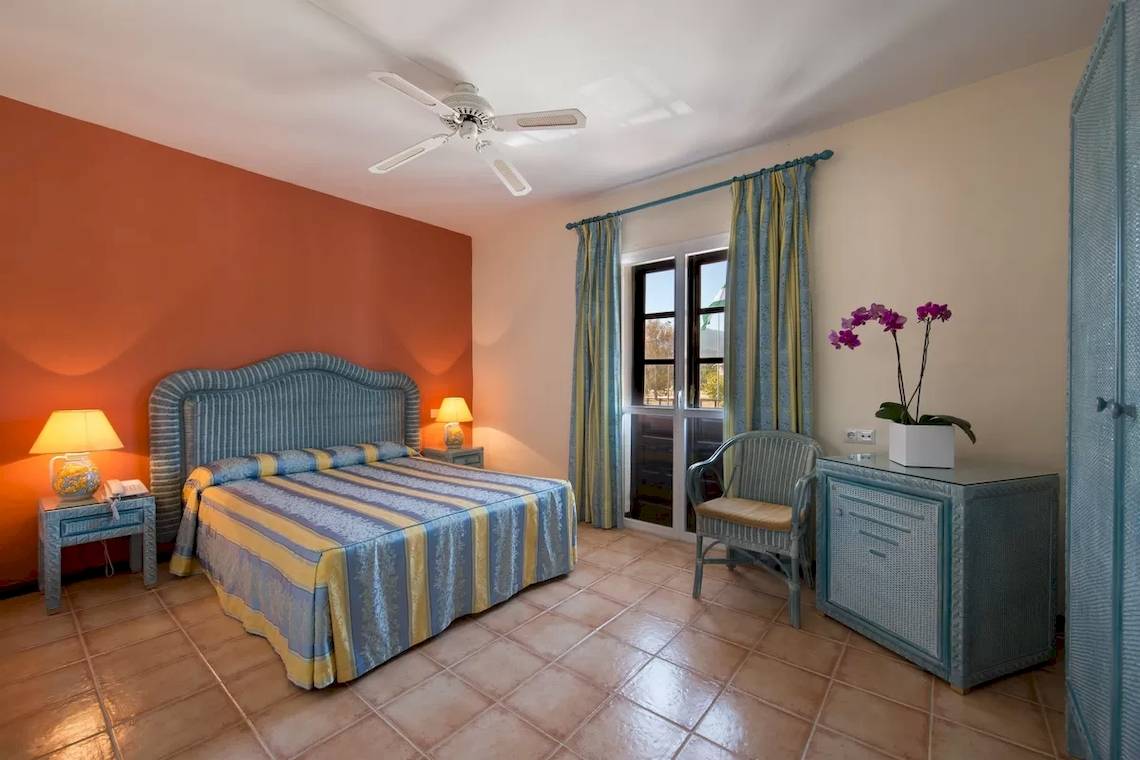 Schlafzimmer im Bluebay Banus Hotel mit Bett, Stuhl, Tisch und Fenster.