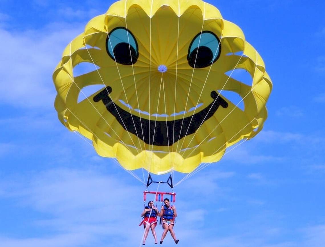 Zwei Leute im Parasailing mit gelber Parasegel mit Smiley-Gesicht.