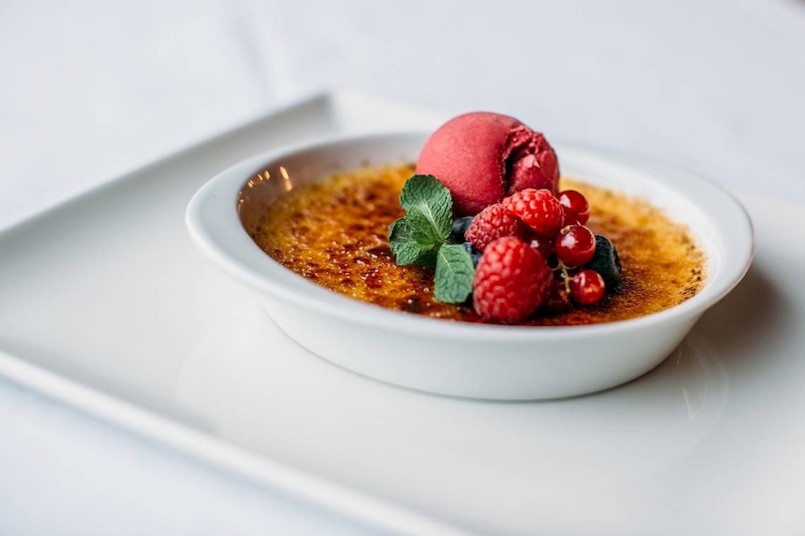 Crème Brûlée in einer weißen Schüssel auf einem weißen Teller mit Früchten und Eis.