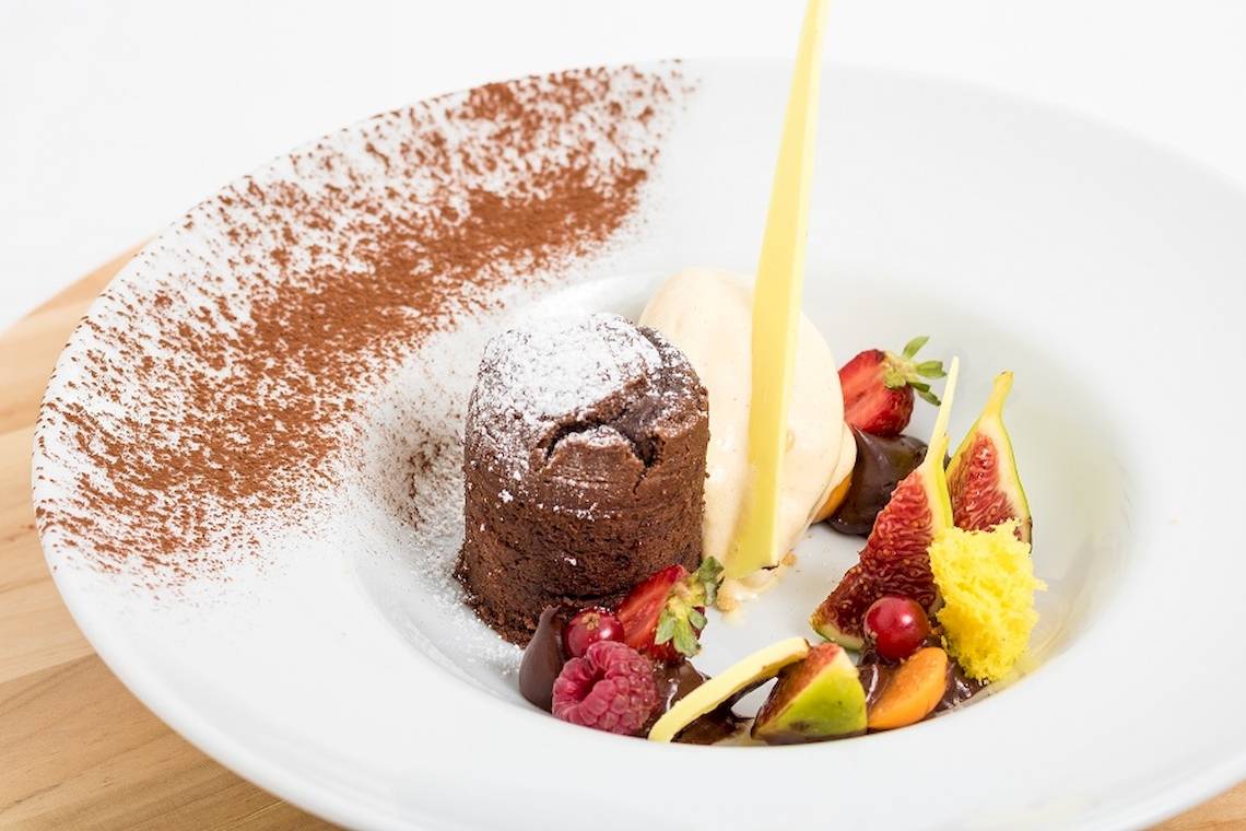 Ein Schokoladenkuchen mit Früchten und Eiscreme auf einem weißen Teller.