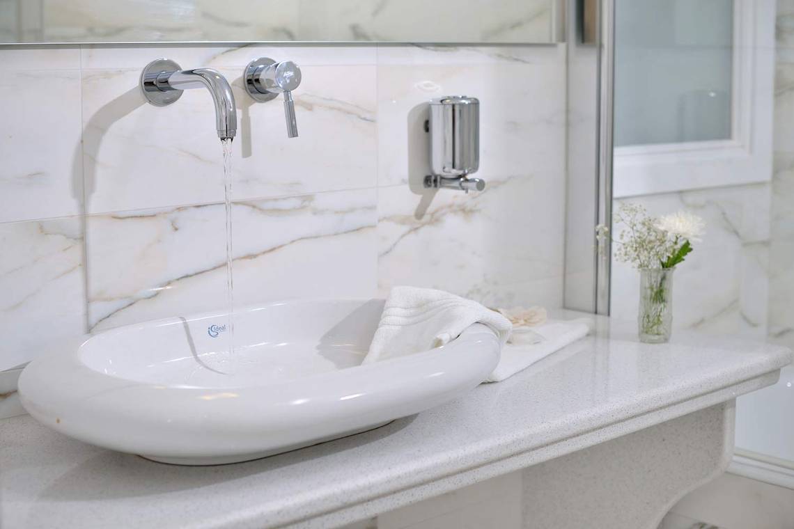 Ein Badezimmer mit einem weißen Waschbecken, das an eine Wand mit Marmorfliesen angeschlossen ist.