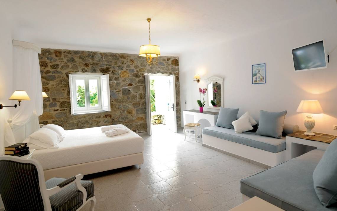 Kamari Hotel Schlafzimmer mit Doppelbett und Sofa, Steinwand, weißer Bettwäsche und Deko