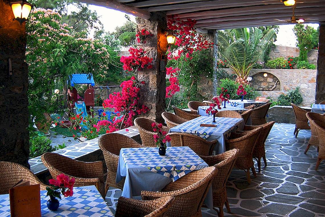 Restaurantterrasse des Kamari Hotels mit Tischen und Stühlen, umgeben von Blumen und Pflanzen.