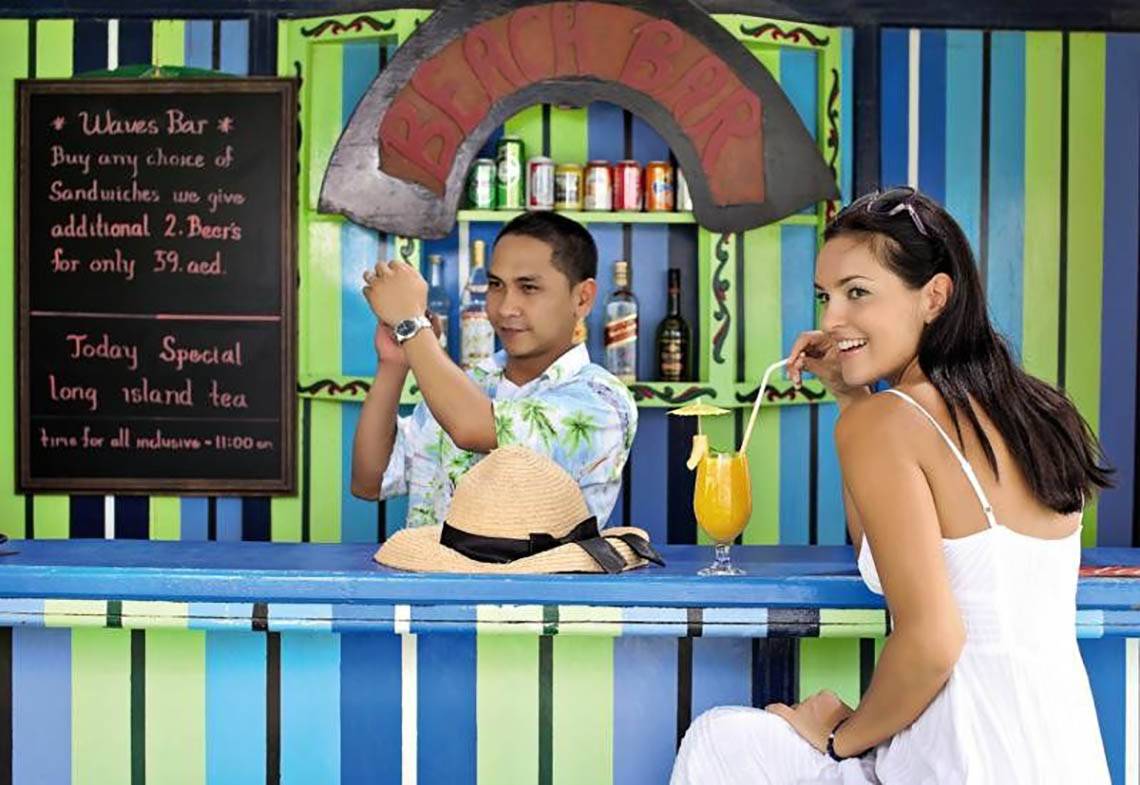 Mann und Frau sitzen an einer Bar im BM Beach Hotel mit Getränken und Blick auf das Menü.