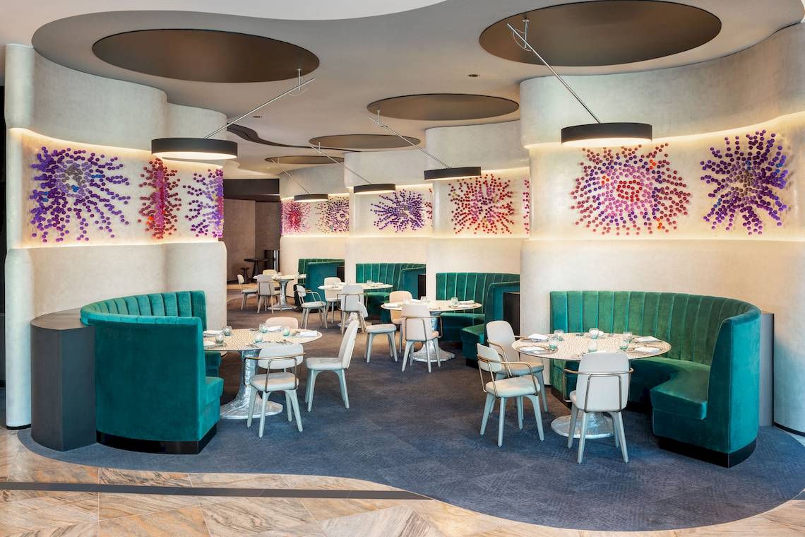 Innenbereich des Restaurants im W Dubai - The Palm mit runden Tischen und blauen Sitzbänken.