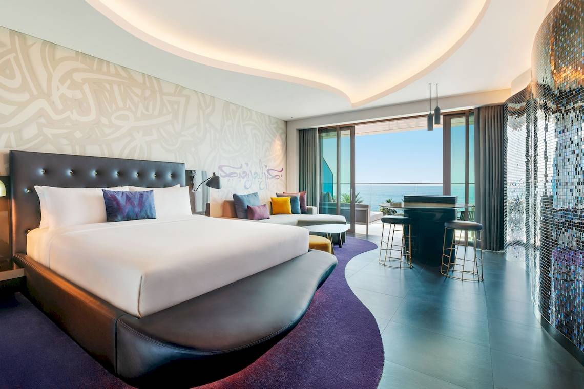 Innenansicht eines Hotelzimmers im W Dubai - The Palm mit Bett, Sofas und Meerblick.