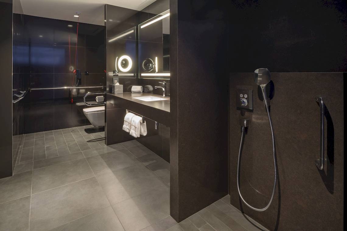 Badezimmer im W Dubai - The Palm Hotel mit schwarzen Wänden, gefliestem Boden und moderner Duschvorrichtung.