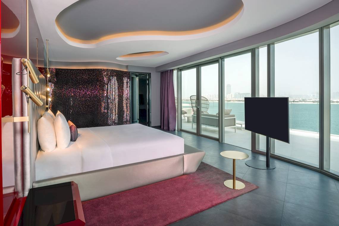 Innenansicht eines Zimmers im W Dubai - The Palm Hotel mit großem Bett, Glaswänden und Meerblick.