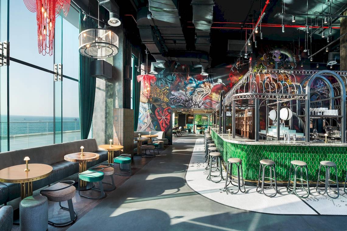Innenansicht des W Dubai - The Palm Hotels mit Bar, Tischen, Stühlen und farbenfrohen Wandgemälden.