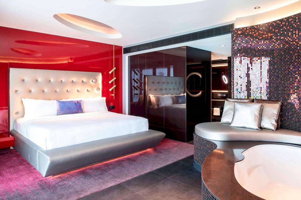 Schlafzimmer im W Dubai - The Palm Hotel mit rotem Wanddesign, silbernem Bett und Badewanne.