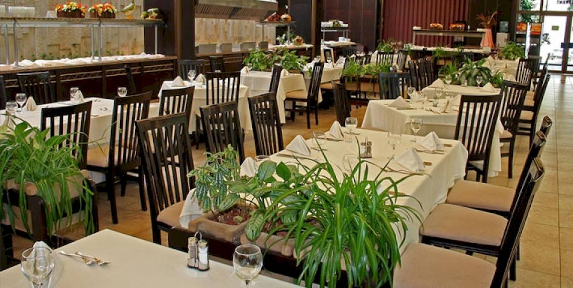 Eine Reihe von gedeckten Tischen und Stühlen in einem Restaurant, mit Pflanzen und gerahmten Bildern an der Wand.