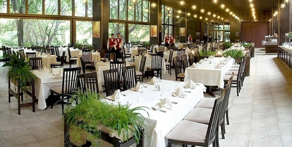 Hotelfoyer mit gedeckten Tischen und Sesseln, zwei Angestellte in roten Westen stehen im Hintergrund.