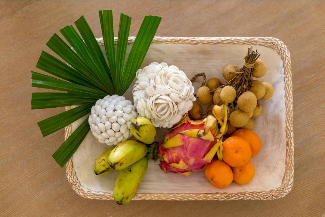 Obst und Blumen in einem Korb auf einem Holztisch, darunter Drachenfrüchte, Bananen und Orangen.