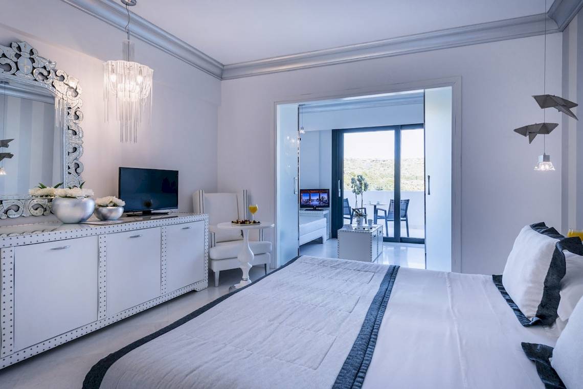 Das Schlafzimmer im Mitsis Alila Resort & Spa mit einem großen Bett, einer Kommode, einem Fernseher und einem Spiegel.