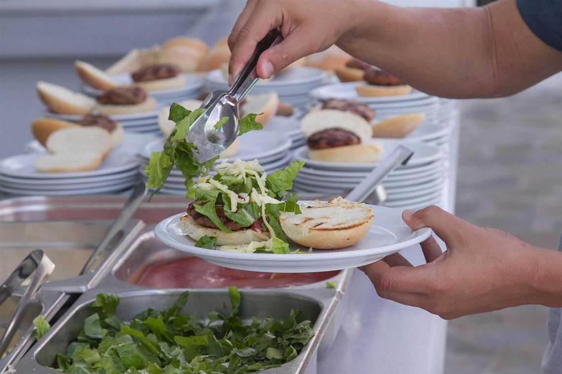 Eine Person serviert einen Burger auf einem weißen Teller in einem Buffet.