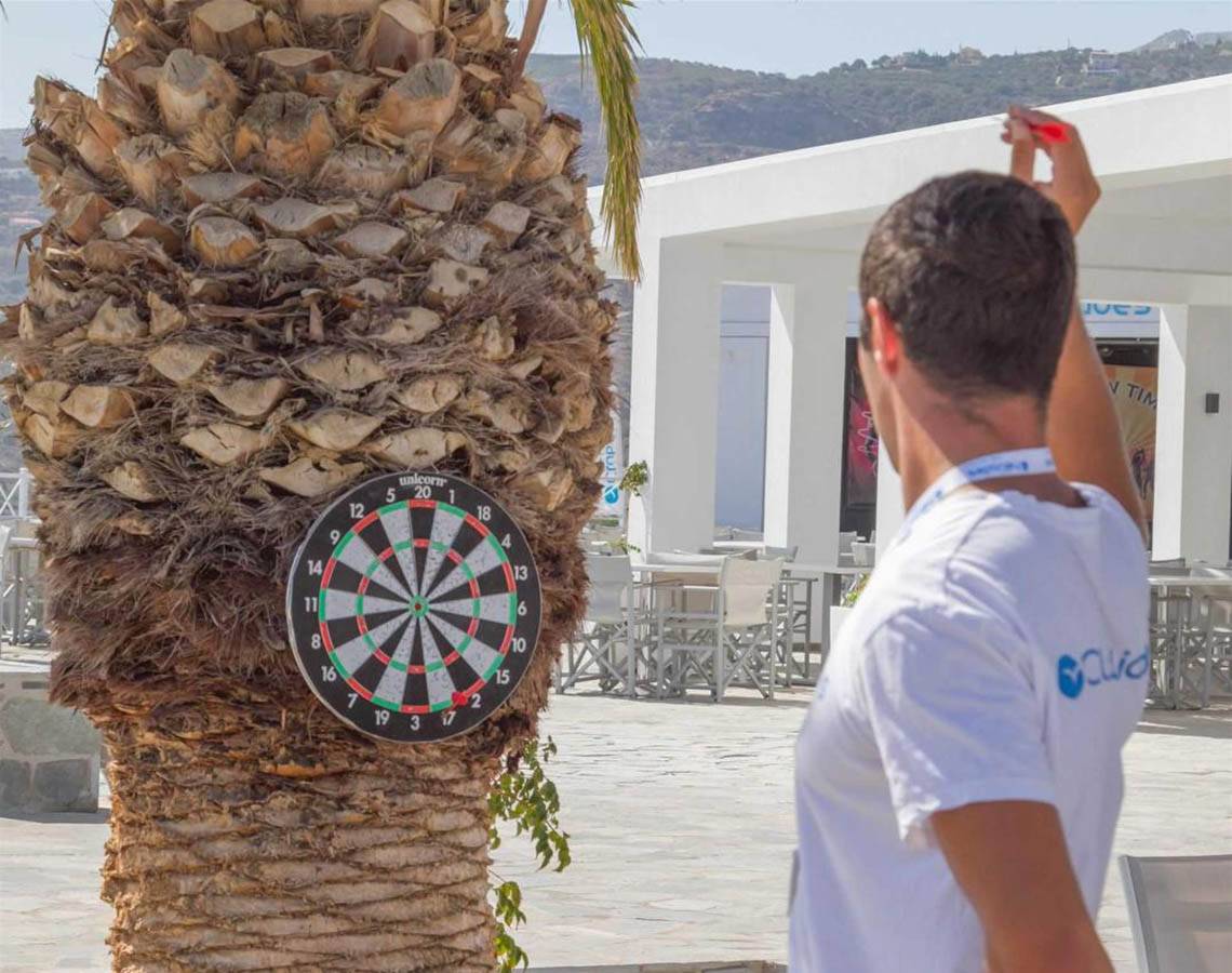 Mann wirft einen Dart auf eine Zielscheibe, die an einer Palme befestigt ist.