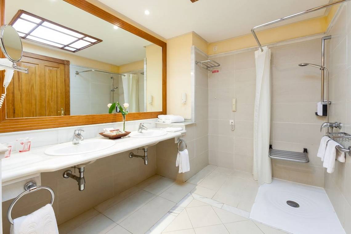 Badezimmer im GF Gran Costa Adeje Hotel mit zwei Waschbecken, großer Spiegel und Dusche.