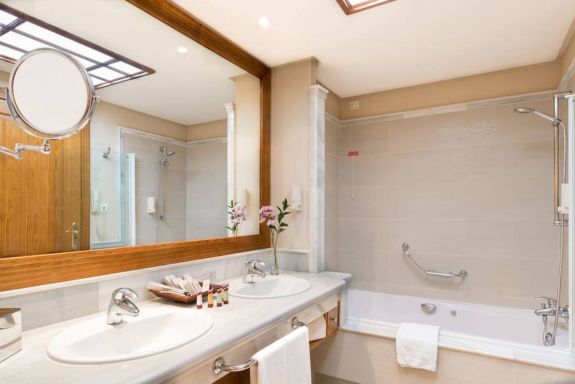Badezimmer im GF Gran Costa Adeje Hotel mit zwei Waschbecken, Spiegel und Badewanne.