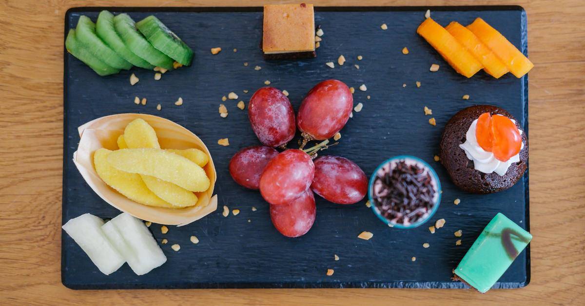 Verschiedene Obstsorten und Snacks auf einem schwarzen Tablett auf einem Holztisch.