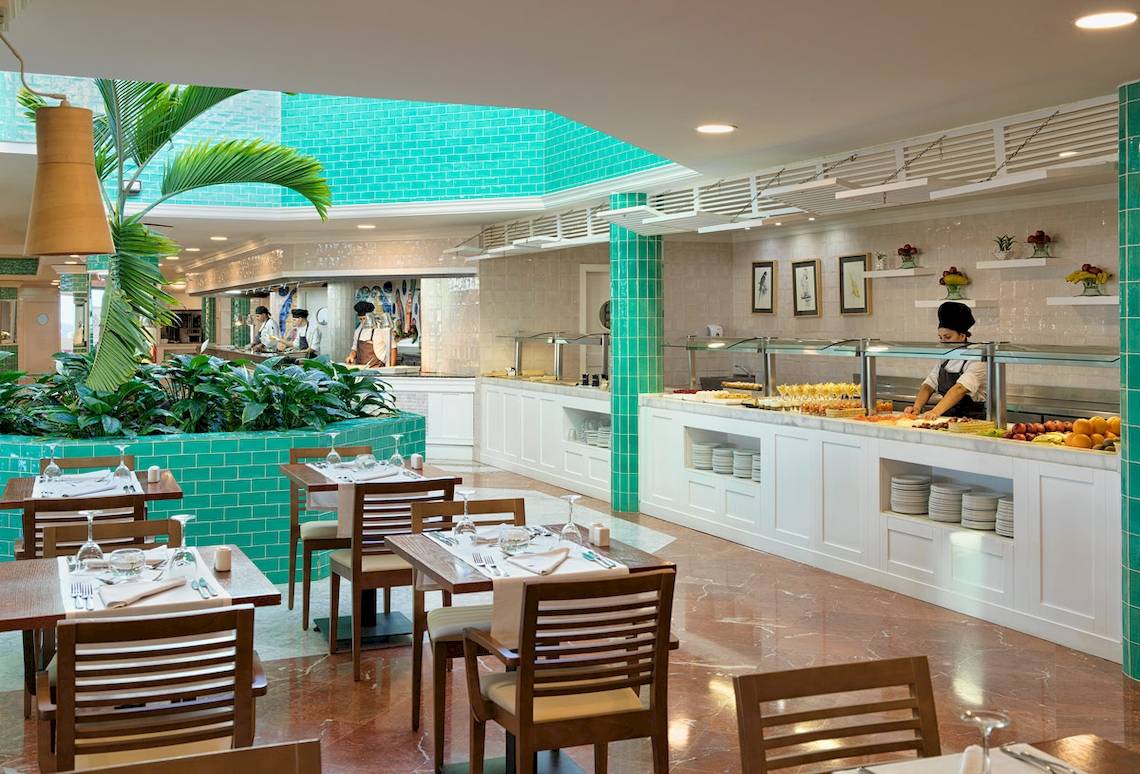 Restaurant im H10 Playa Esmeralda Hotel mit grünen Wänden und blauen Fliesen, servierenden Kellnern und gedeckten Tischen.