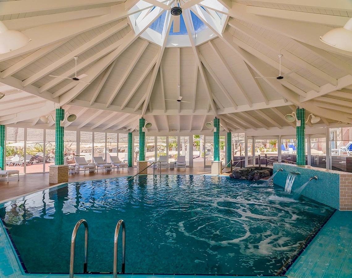 Innenbereich des Poolbereichs im H10 Playa Esmeralda Hotel mit Glasdach und grünen Säulen