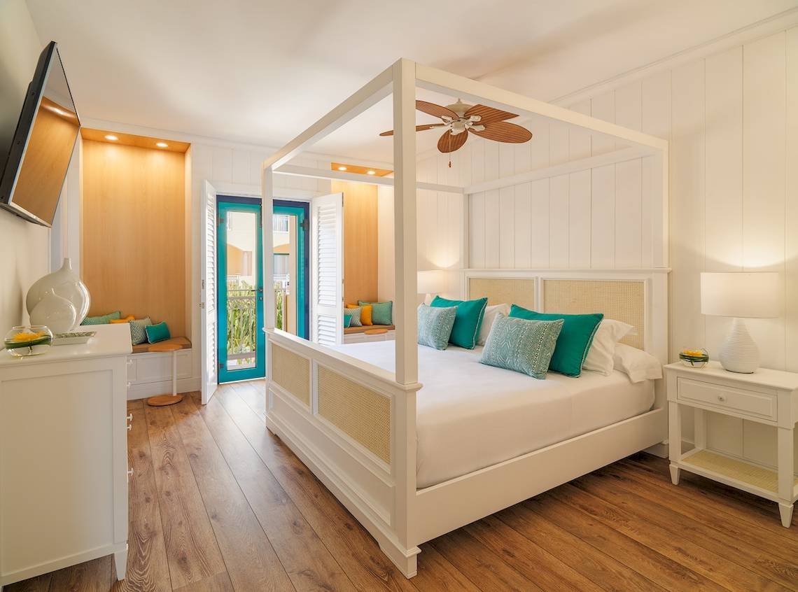 Schlafzimmer im H10 Playa Esmeralda Hotel mit einem Himmelbett, weißem Bettzeug und grünen Kissen.