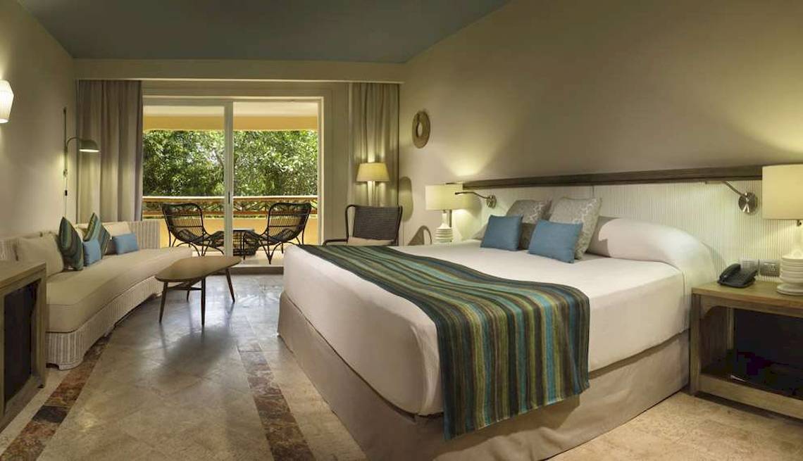 Ein modernes Hotelzimmer im Catalonia Royal Tulum mit einem großen Bett, einem Sofa und einem Balkon mit Möbeln.