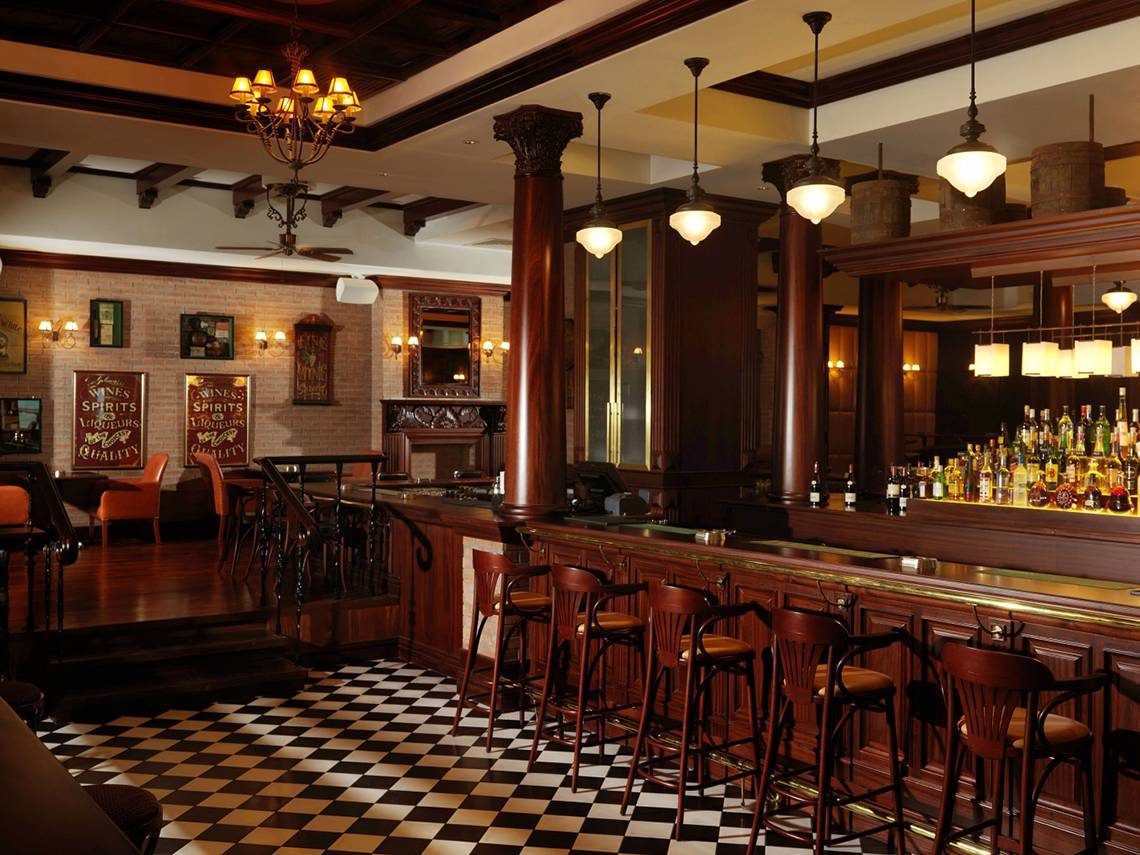 Innenansicht der Bar im Park Rotana Abu Dhabi Hotel mit Holzboden, Barhockern und einer Bartheke mit Flaschen.